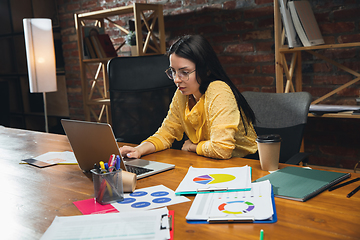 Image showing Young woman working in modern office using devices and gadgets. Making reports, analitycs, routine processing tasks