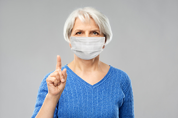 Image showing senior woman in medical mask pointing finger up