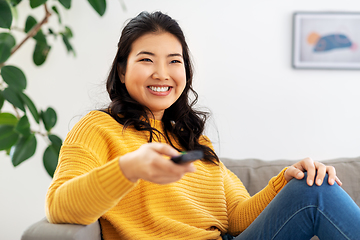 Image showing asian woman with tv remote sitting on sofa at home