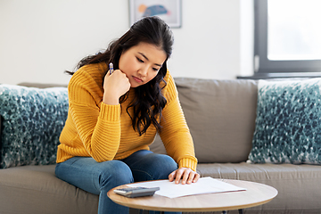 Image showing sad asian woman with papers and calculator at home