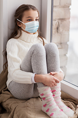 Image showing sad girl in medical mask sitting on sill at home