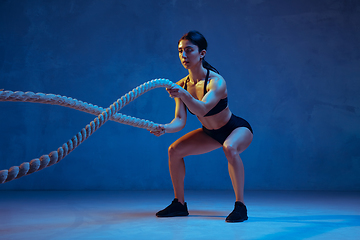 Image showing Caucasian young female athlete practicing on blue studio background in neon light