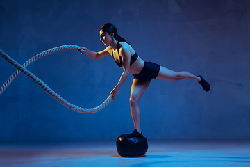 Image showing Caucasian young female athlete practicing on blue studio background in neon light