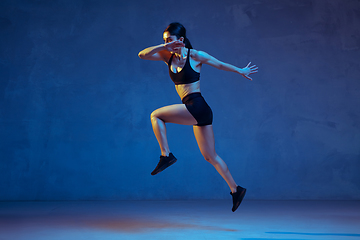 Image showing Caucasian young female athlete practicing on blue studio background in neon light