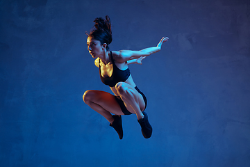 Image showing Caucasian young female athlete practicing on blue studio background in neon light