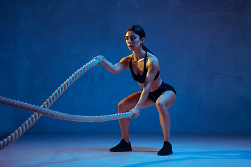 Image showing Caucasian young female athlete practicing on blue studio background in neon light