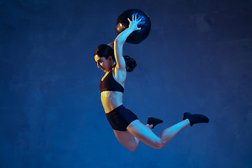 Image showing Caucasian young female athlete practicing on blue studio background in neon light