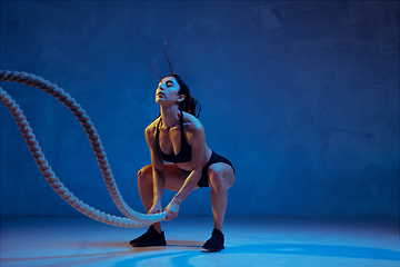 Image showing Caucasian young female athlete practicing on blue studio background in neon light