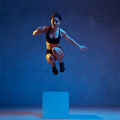 Image showing Caucasian young female athlete practicing on blue studio background in neon light