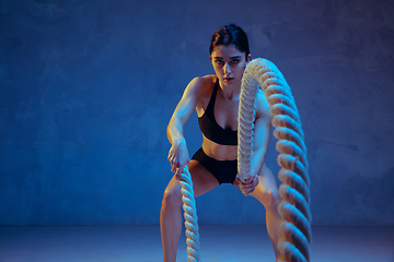 Image showing Caucasian young female athlete practicing on blue studio background in neon light