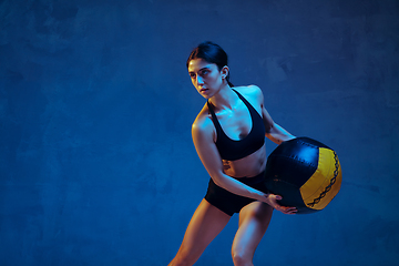 Image showing Caucasian young female athlete practicing on blue studio background in neon light