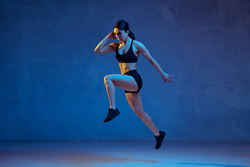 Image showing Caucasian young female athlete practicing on blue studio background in neon light