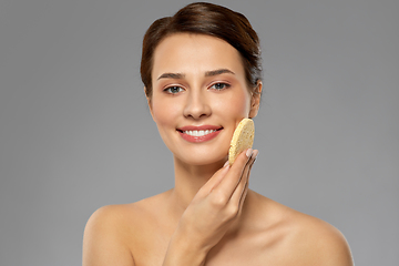 Image showing young woman cleaning face with exfoliating sponge