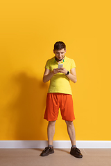 Image showing Young caucasian man using smartphone. Full body length portrait isolated over yellow background.