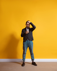 Image showing Young caucasian man using smartphone. Full body length portrait isolated over yellow background.