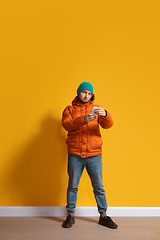 Image showing Young caucasian man using smartphone. Full body length portrait isolated over yellow background.