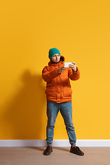 Image showing Young caucasian man using smartphone. Full body length portrait isolated over yellow background.