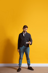 Image showing Young caucasian man using smartphone. Full body length portrait isolated over yellow background.