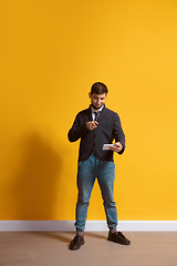 Image showing Young caucasian man using smartphone. Full body length portrait isolated over yellow background.