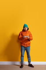 Image showing Young caucasian man using smartphone. Full body length portrait isolated over yellow background.