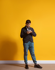 Image showing Young caucasian man using smartphone. Full body length portrait isolated over yellow background.