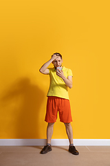 Image showing Young caucasian man using smartphone. Full body length portrait isolated over yellow background.