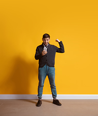 Image showing Young caucasian man using smartphone. Full body length portrait isolated over yellow background.