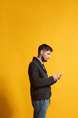 Image showing Young caucasian man using smartphone. Full body length portrait isolated over yellow background.