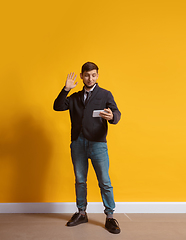 Image showing Young caucasian man using smartphone. Full body length portrait isolated over yellow background.