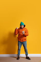 Image showing Young caucasian man using smartphone. Full body length portrait isolated over yellow background.