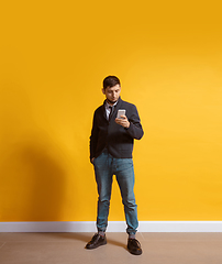 Image showing Young caucasian man using smartphone. Full body length portrait isolated over yellow background.