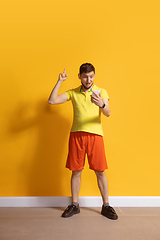 Image showing Young caucasian man using smartphone. Full body length portrait isolated over yellow background.