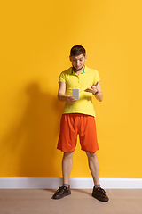 Image showing Young caucasian man using smartphone. Full body length portrait isolated over yellow background.