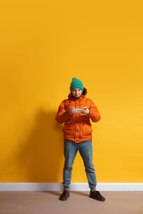 Image showing Young caucasian man using smartphone. Full body length portrait isolated over yellow background.