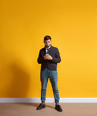 Image showing Young caucasian man using smartphone. Full body length portrait isolated over yellow background.