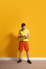 Image showing Young caucasian man using smartphone. Full body length portrait isolated over yellow background.