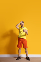 Image showing Young caucasian man using smartphone. Full body length portrait isolated over yellow background.