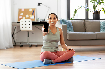 Image showing woman with smartphone sits on exercise mat at home