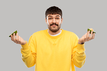 Image showing confused young man with avocado shrugging