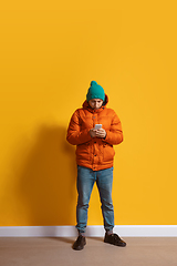 Image showing Young caucasian man using smartphone. Full body length portrait isolated over yellow background.