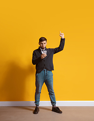 Image showing Young caucasian man using smartphone. Full body length portrait isolated over yellow background.