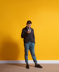 Image showing Young caucasian man using smartphone. Full body length portrait isolated over yellow background.