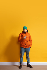 Image showing Young caucasian man using smartphone. Full body length portrait isolated over yellow background.