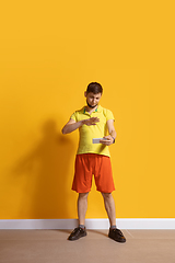 Image showing Young caucasian man using smartphone. Full body length portrait isolated over yellow background.