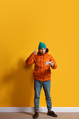 Image showing Young caucasian man using smartphone. Full body length portrait isolated over yellow background.