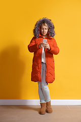 Image showing Young caucasian woman using smartphone. Full body length portrait isolated over yellow background.