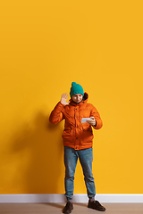 Image showing Young caucasian man using smartphone. Full body length portrait isolated over yellow background.