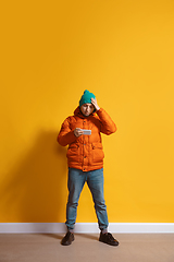 Image showing Young caucasian man using smartphone. Full body length portrait isolated over yellow background.