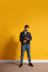 Image showing Young caucasian man using smartphone. Full body length portrait isolated over yellow background.