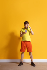 Image showing Young caucasian man using smartphone. Full body length portrait isolated over yellow background.